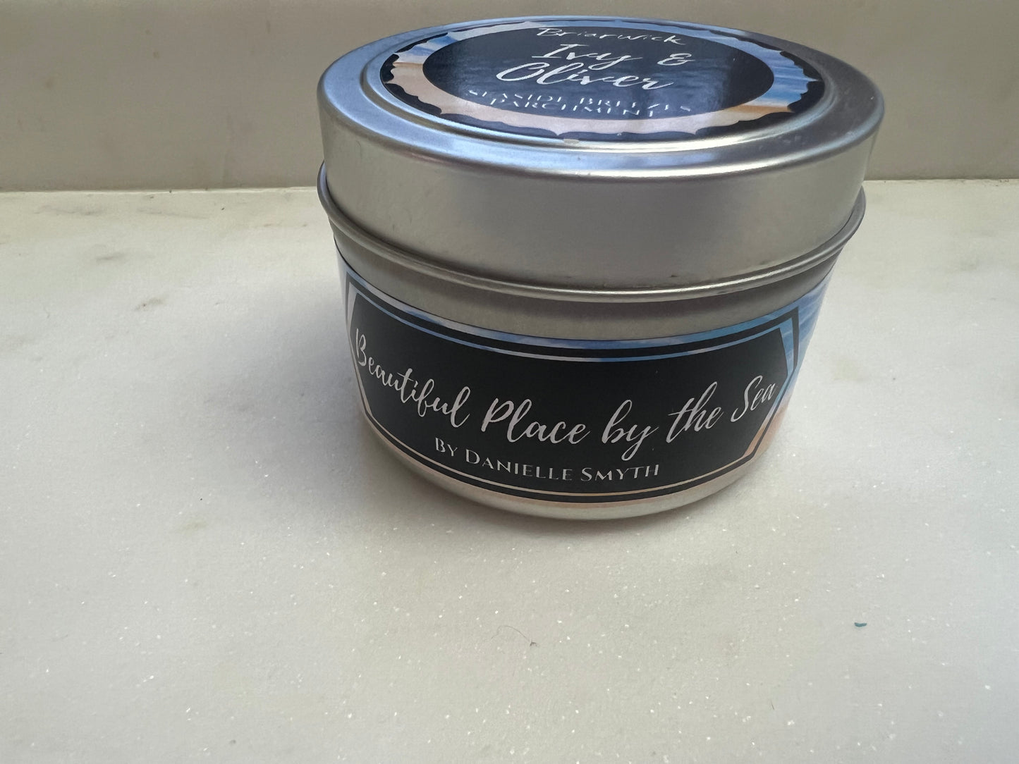 Candle in a metal tin with a label on a white surface