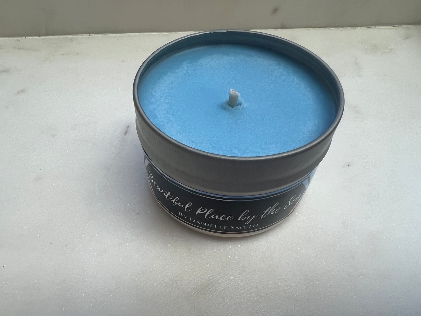 Blue candle in a tin container on a white surface